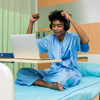 Teenager sitting in a hospital room with a laptop.