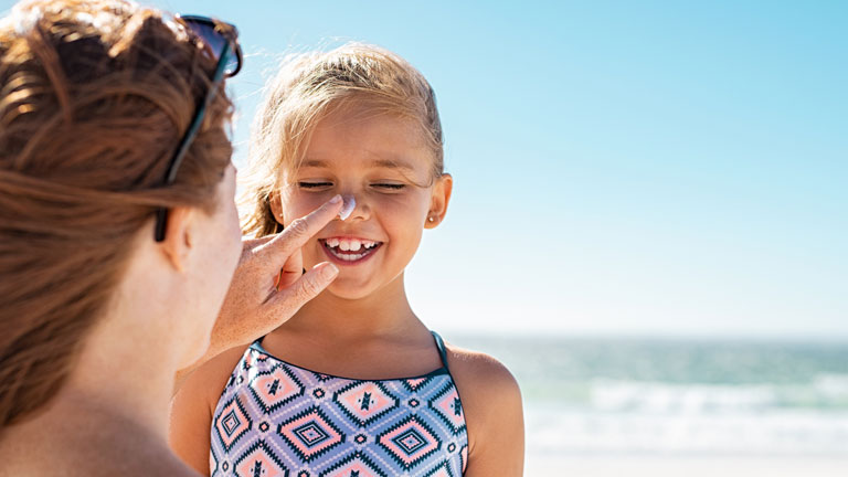 A parent reapplies sunscreen to a young child on the beach