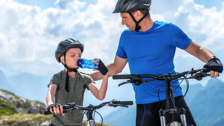 A father gives a child water during a bike ride on a hot day