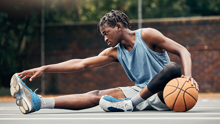 Male teen basketball player stretching.